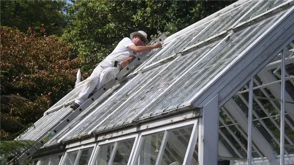 Мужчина ремонтирует крышу на теплице